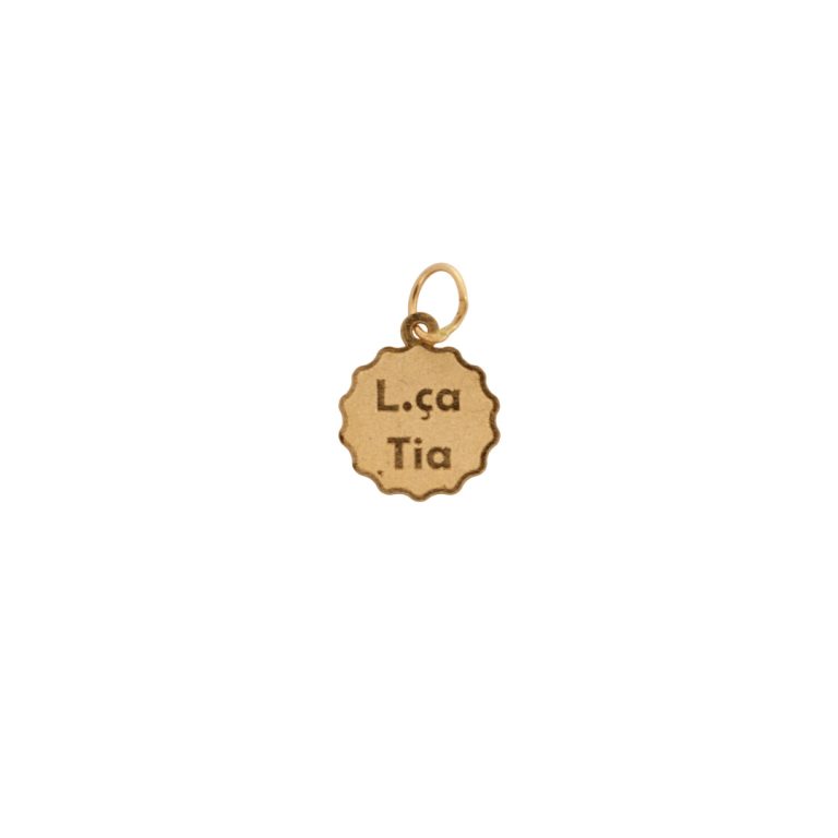 Medalha de ouro em forma de flor com a inscrição “Lç.ª Tia”.